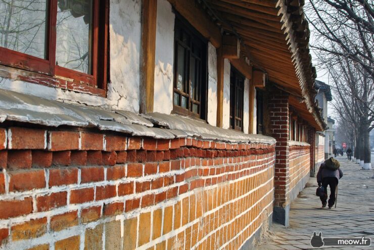 Old brick building with wooden roof, large windows, and person walking - urban scene.