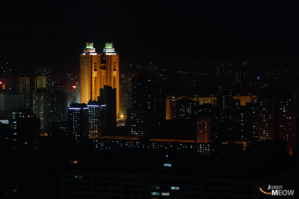 Nighttime cityscape of modern Pyongyang, North Korea, with glowing skyscrapers along the Taedong River.