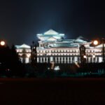 Night skyline of Pyongyang, North Korea with grand illuminated building and lush greenery.