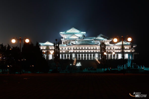 Night skyline of Pyongyang, North Korea with grand illuminated building and lush greenery.