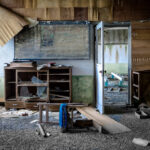 Abandoned classroom on Gunkanjima Island: decaying furniture, haunting atmosphere of forgotten mining community.