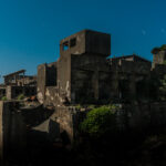 Abandoned coal mining town on Gunkanjima island at night, eerie, decaying industrial buildings.