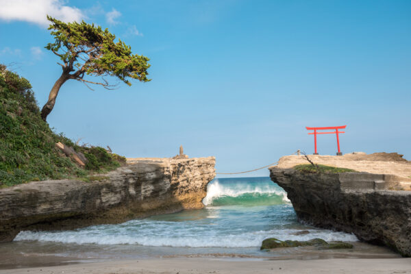 Tranquil coastal scene with red torii gate, vibrant turquoise waters, and dramatic rock formation.