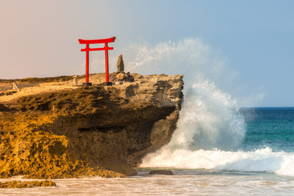 Majestic Japanese torii gate on rocky promontory overlooking ocean waves.