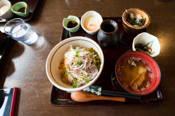 Traditional Japanese breakfast spread with rice, soup, and veggies on wooden tray.