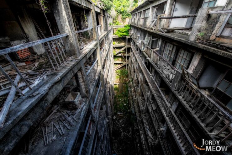 Decaying pathway with abandoned structure, overgrown vegetation, and sunlight filtering through cracks.