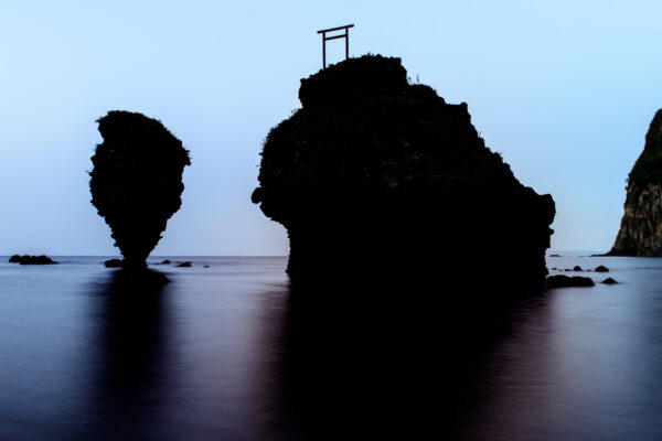 Tranquil coastal landscape at dusk with majestic Ebisu & Daikoku rocks and a torii gate.