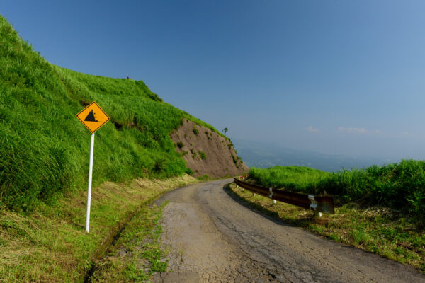 Tranquil mountain road through lush hills under clear blue sky.