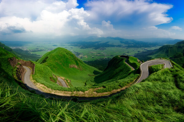 Breathtaking view of winding mountain road in Aso Valley, surrounded by lush green hills.