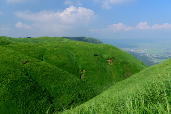 Tranquil mountain road through lush green hills under a hazy blue sky.