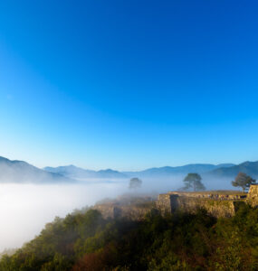 Takeda Castle in Japan, shrouded in mist, against a backdrop of lush greenery.