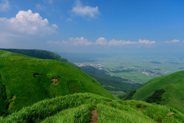 Mystical Mountain Road Through Lush Green Hills, Tranquil Landscape with City in Distance.