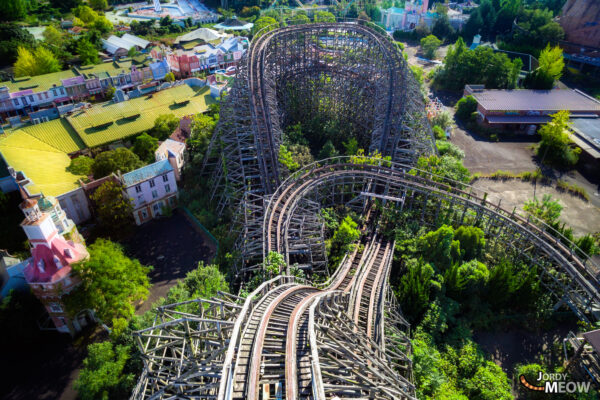 Aerial view of abandoned Nara Dreamland theme park, showcasing decaying roller coaster and colorful buildings.