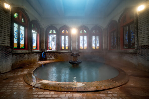 Serene Japanese ryokan with hot spring pool, featuring high ceilings, arched windows, and brick walls.