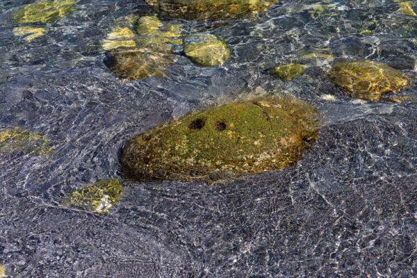 Tranquil Shikinejima island oasis, mossy rocks amidst turquoise shallows.