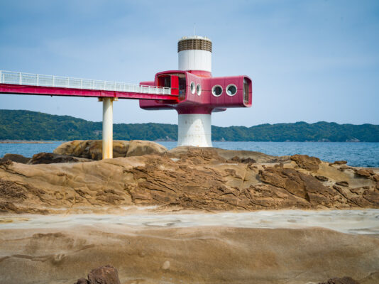 Distinctive red-white seaside lighthouse on rocky coast.