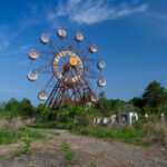Rusty Ferris wheel in overgrown abandoned amusement park under blue sky