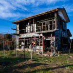 Abandoned black two-story house covered in graffiti beneath a bright blue sky