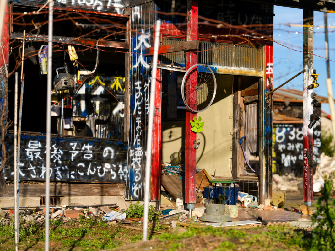 Scorched ruined house with Japanese graffiti, exposed interior debris, and grass regrowth