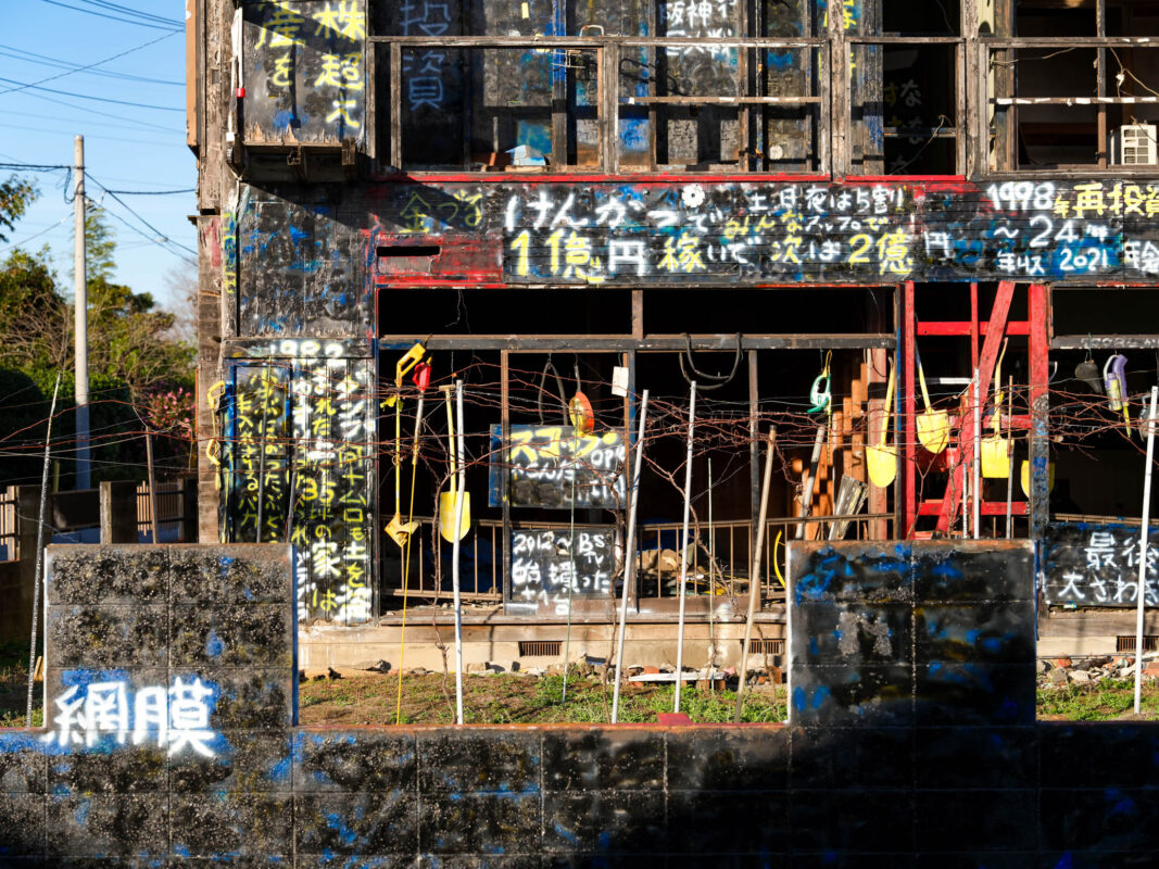 Weathered black house covered in Japanese graffiti, red beam, concrete wall, bright blue sky.