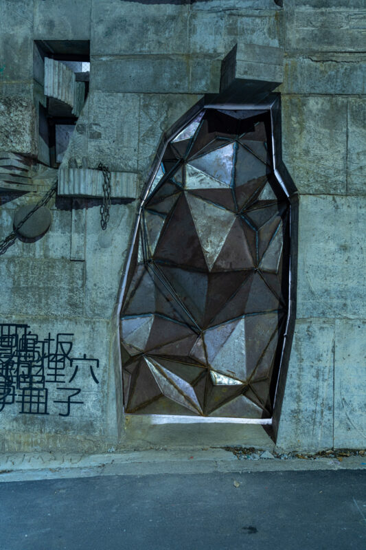 Low-poly metal bear sculpture embedded in weathered concrete wall with Japanese graffiti