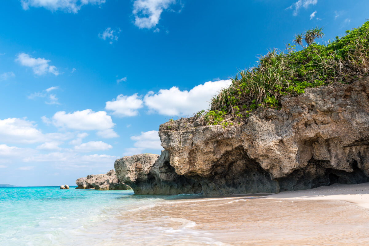 Miyako Island beach with turquoise water, white sand, and limestone cliffs under blue sky.