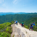 Hikers on Mount Ōdaigahara ridge trail overlooking forested mountains in Japan
