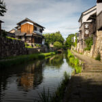Omihachiman canal in Japan lined with traditional wooden townhouses and a stone walkway.