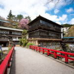 Sekizenkan Ryokan wooden inn beyond red bridge, spring cherry blossoms, Japan