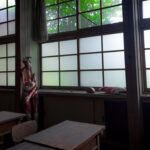 Abandoned classroom with dusty desks and anatomy model by frosted windows, eerie horror atmosphere