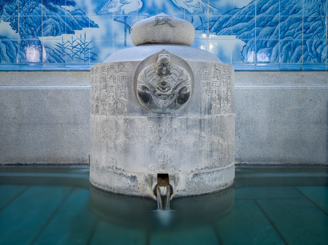 Stone fountain at Dōgo Onsen with turquoise water and blue ceramic tile mural.