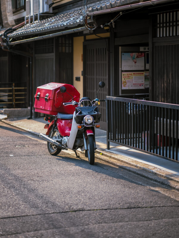 Red delivery scooter parked on a quiet traditional street in Kyoto’s Gion district.