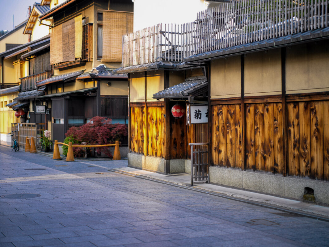 Quiet stone lane in Kyoto Gion with traditional wooden machiya and red lantern.