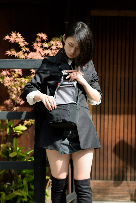 Kyoto street portrait of Masumi adjusting a black bag by traditional wooden slats.