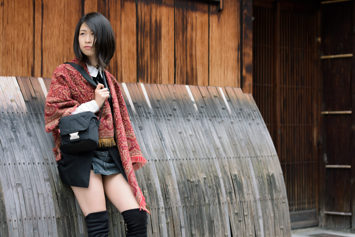 Street style portrait of woman in Kyoto beside curved wooden wall, red patterned shawl