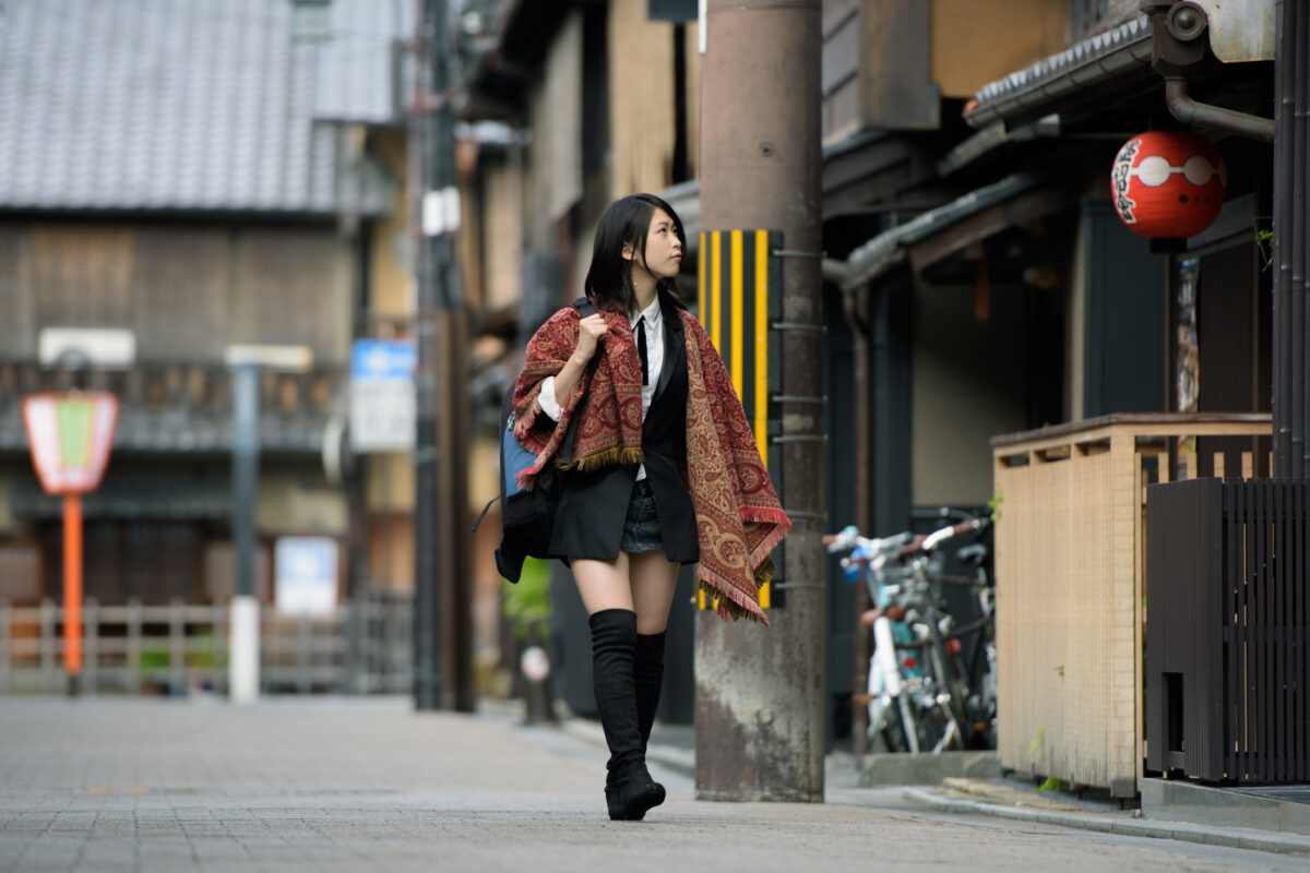 Woman in modern kimono jacket and boots walking a narrow Kyoto street by red lantern