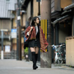 Woman in modern kimono jacket and boots walking a narrow Kyoto street by red lantern