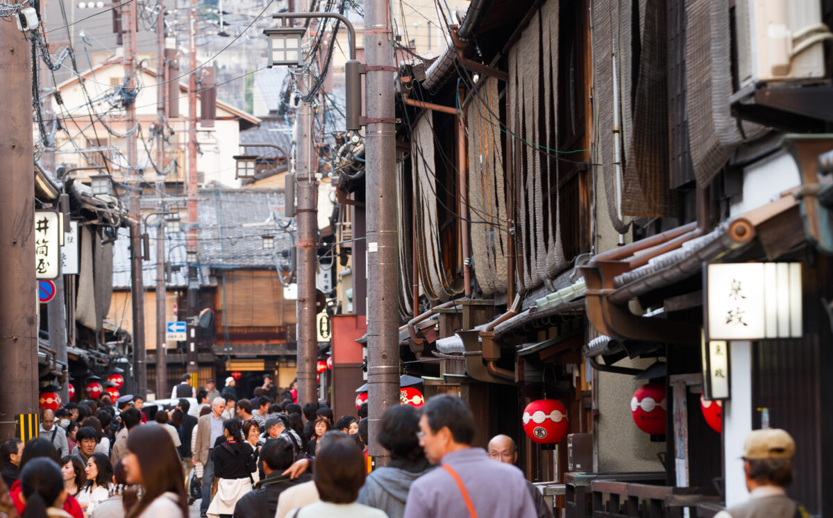Crowded Japanese alley with lantern-lit izakayas, wooden buildings, and overhead power lines
