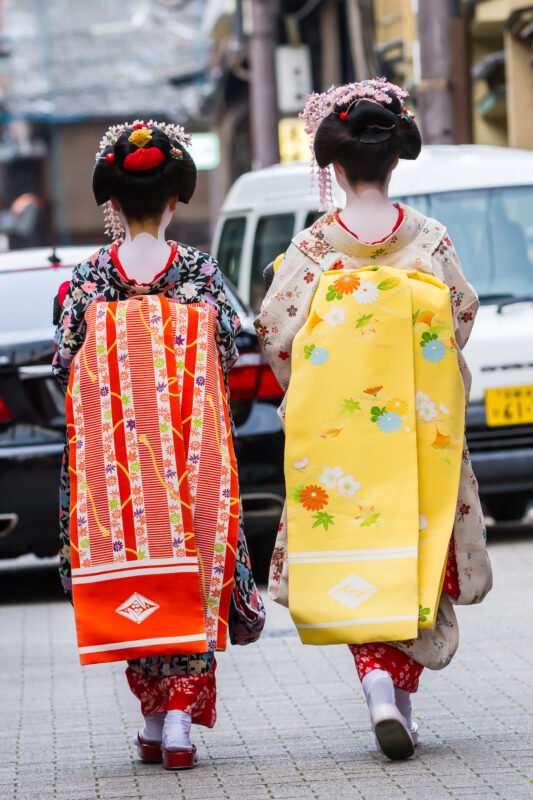 Two women in traditional Japanese kimono walk down a modern city street.