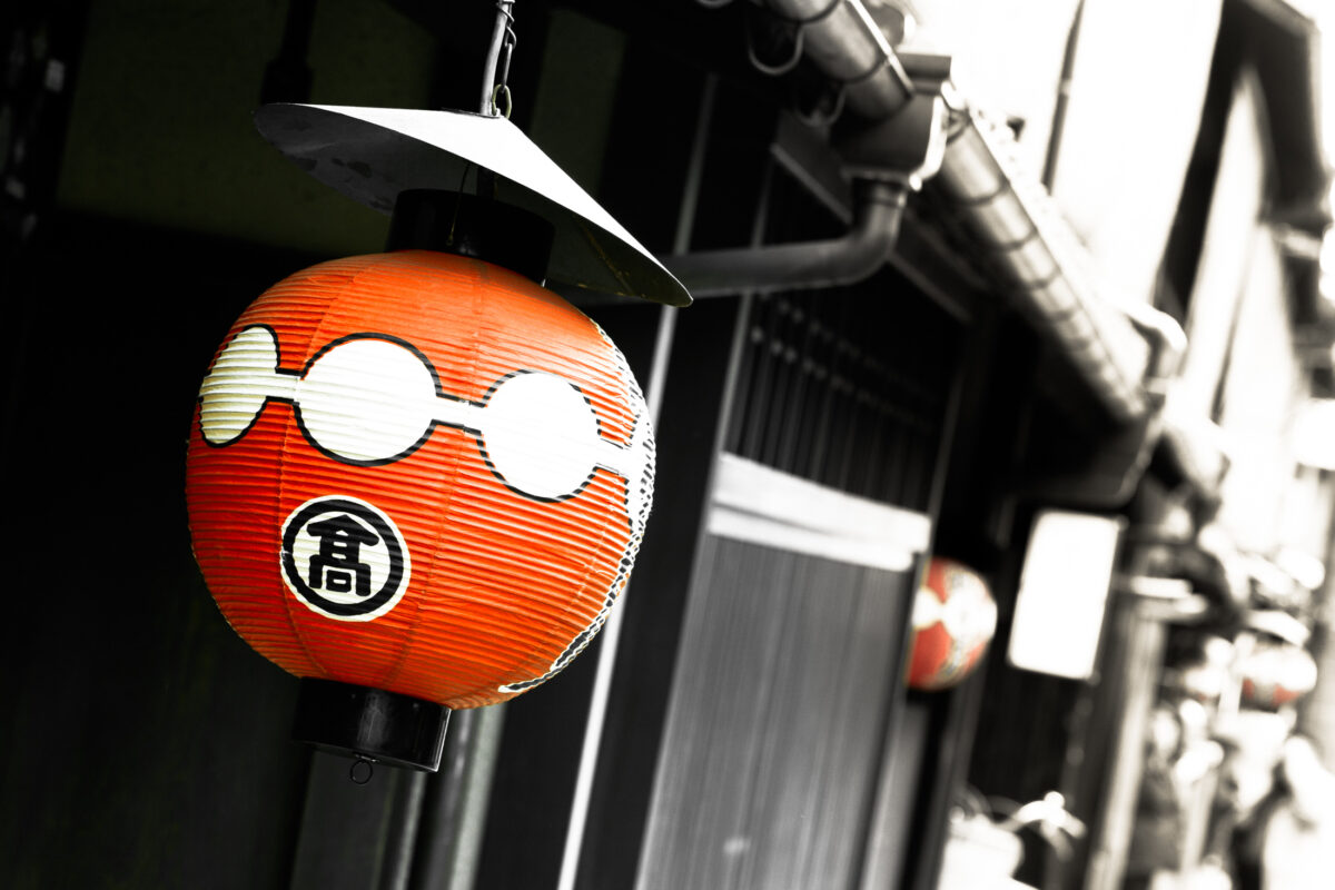 Close-up of weathered red Japanese paper lantern with kanji on traditional wooden streetfront.