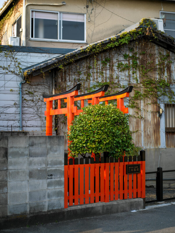 Hidden vermilion torii gate shrine on a narrow street in Kyoto’s Gion district.