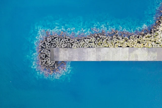 Turquoise waves clash with gray sentinels of concrete— nature's dance with man. 青波が 灰色の守り手と舞う— 自然と人の踊り。#oceanview #tetrapods #seawall #coastaldefense #offbeatjapan #japan #natureandman #aerialphotography