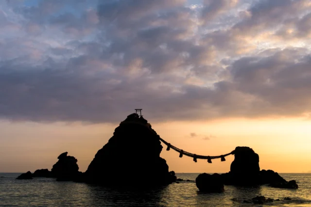 Sunset ocean hues, Wedded Rocks in warm embrace, Harmony of stone. 日没の海、 夫婦岩の抱擁、 石の調和。#MeotoIwa #HarmonyInNature #SereneSunset #CulturalJapan #TravelInspiration #offbeatjapan #japan